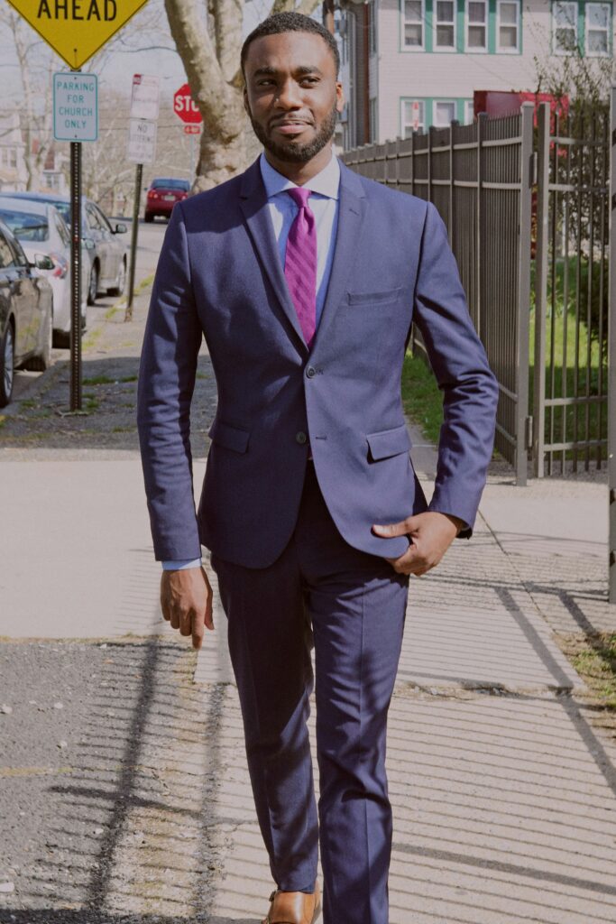 Friendly young black man in a blue suit and tie walking down a city sidewalk